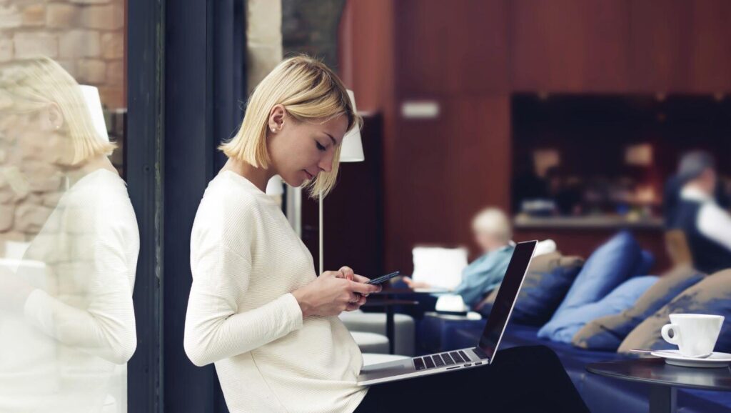 Business woman working on smart phone and laptop computer at a coffee shop