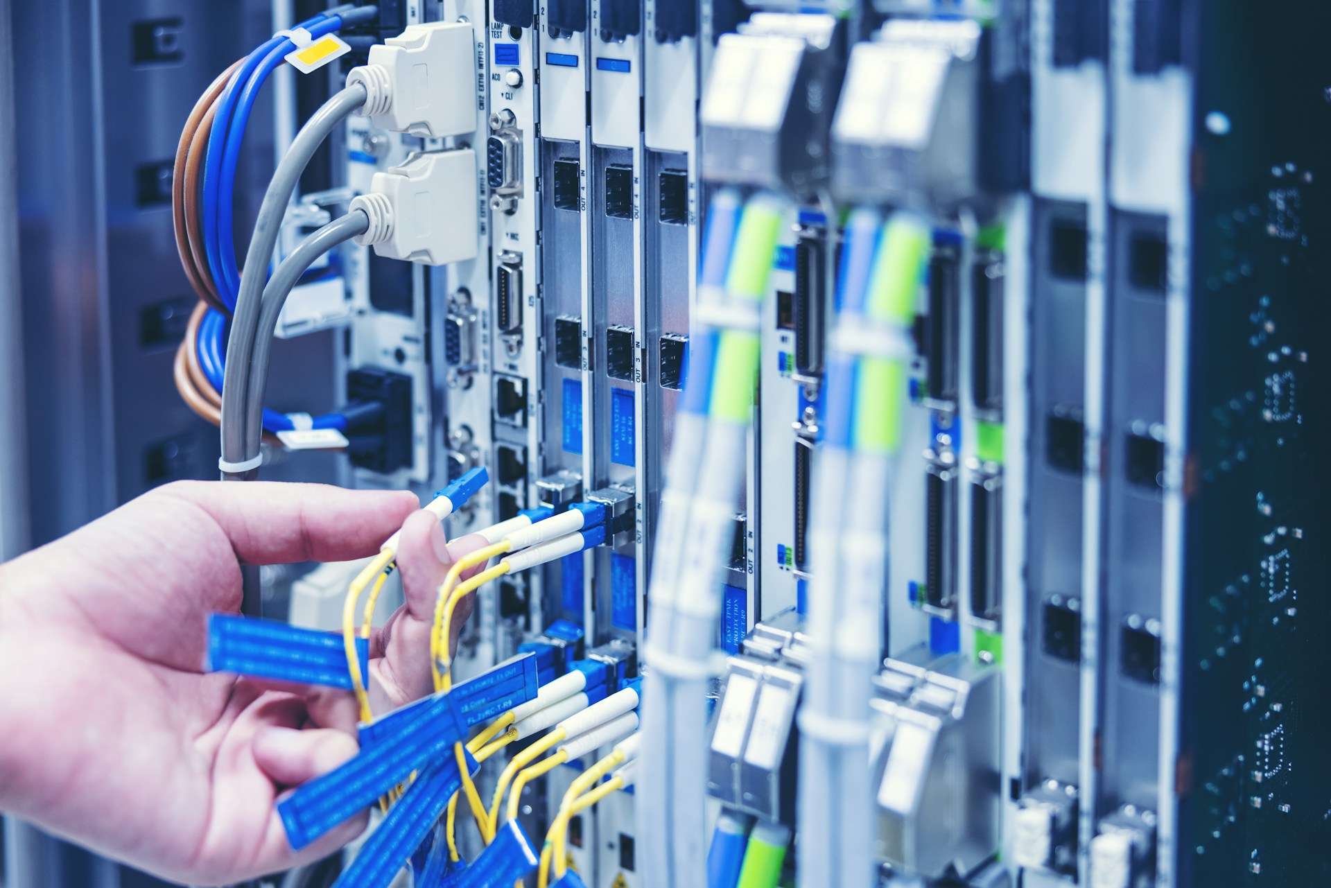 A technician installing structured cabling in a data center, connecting fiber optic and Ethernet cables for a high-performance business network.