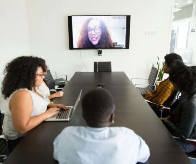 A group of professionals in a conference room on a video call with a remote participant, demonstrating potential audio echo issues in hybrid meetings.