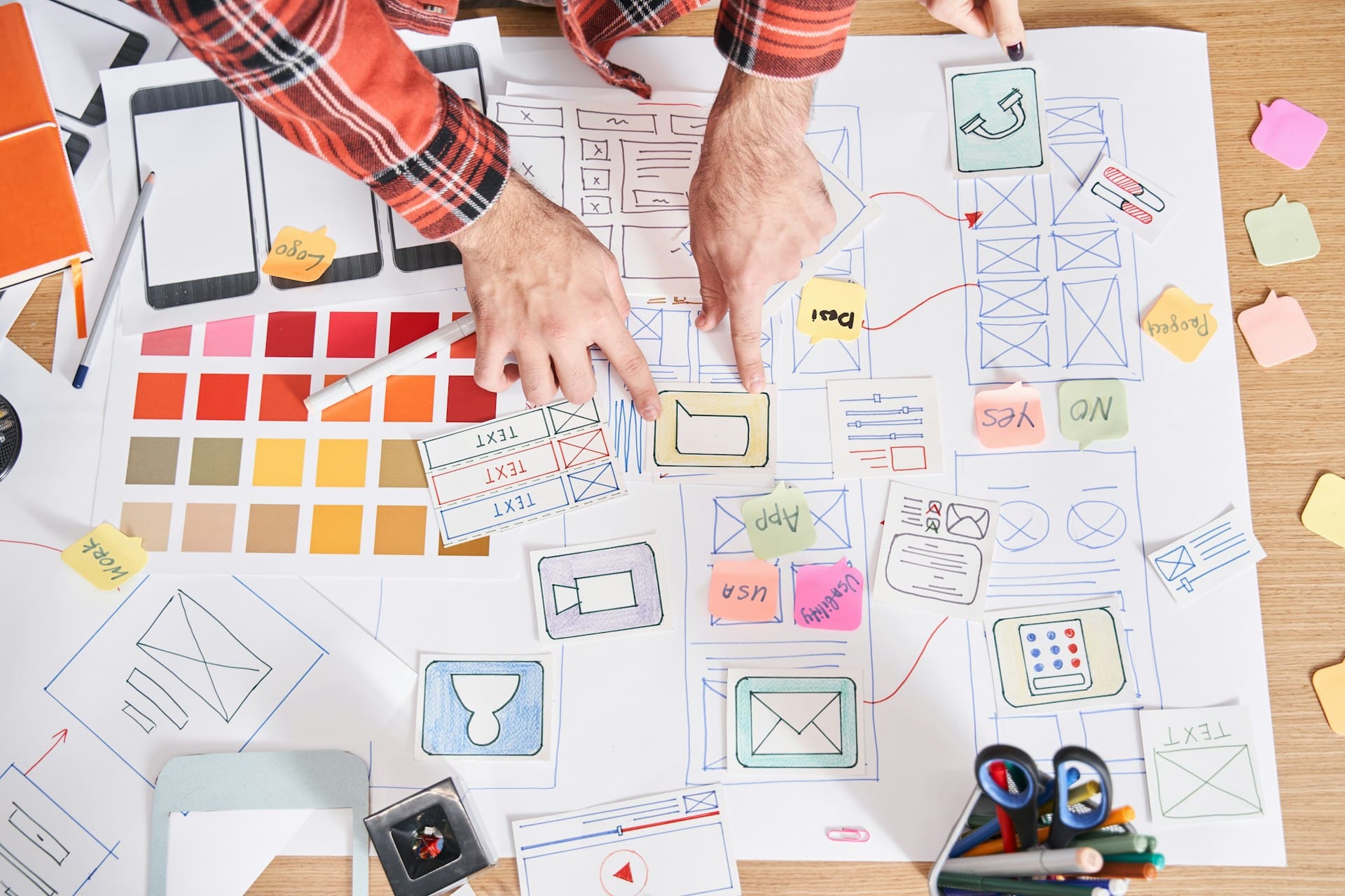 Hands working on an omnichannel customer service strategy with wireframes, color palettes, and design elements for a seamless user experience.