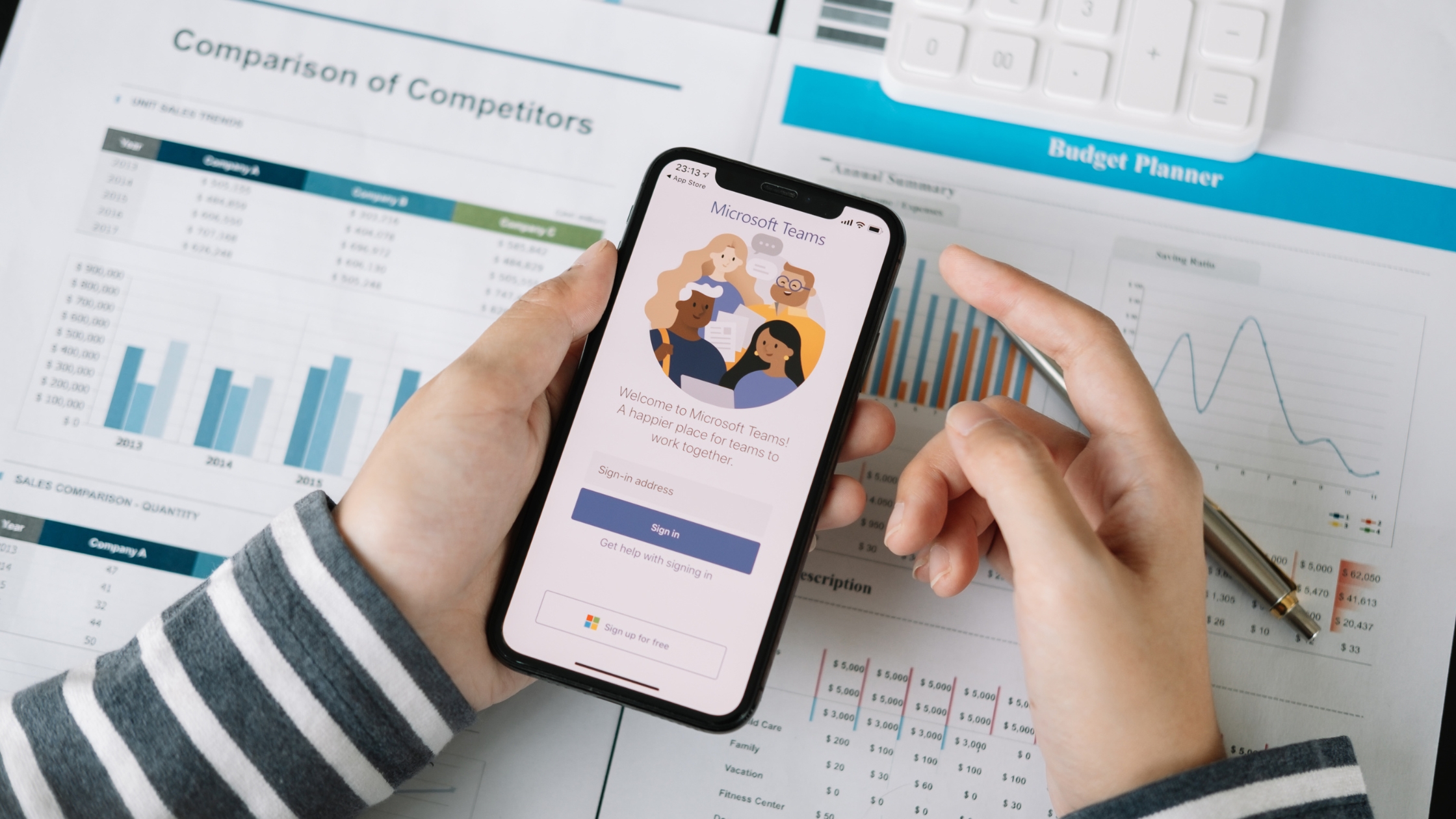 Person holding a smartphone displaying Microsoft Teams login screen, with business performance charts and data in the background, representing call quality and network monitoring solution