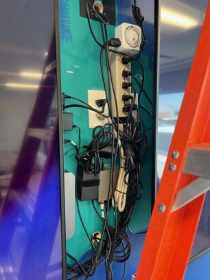 Tangled power cords and device cables behind a wall-mounted display showing an example of bad cable management